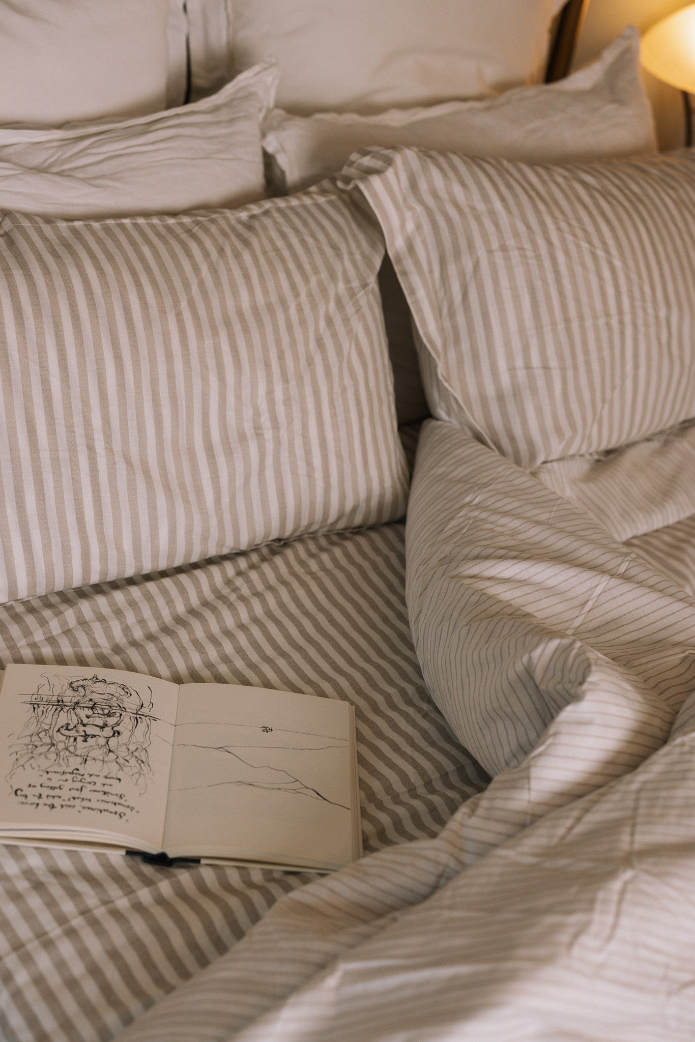 Unmade Striped neutral bedding on a brass bed with an open book.
