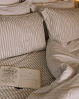 Unmade Striped neutral bedding on a brass bed with an open book.