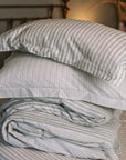 Green striped bedding folded up on a striped bedsheet.