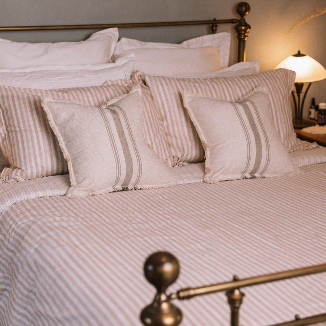 Blush pink striped bedding in a neutral bedroom with a brass bed.