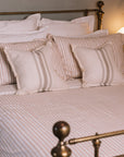 Blush pink striped bedding in a neutral bedroom with a brass bed.