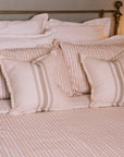 Blush pink striped bedding in a neutral bedroom with a brass bed.