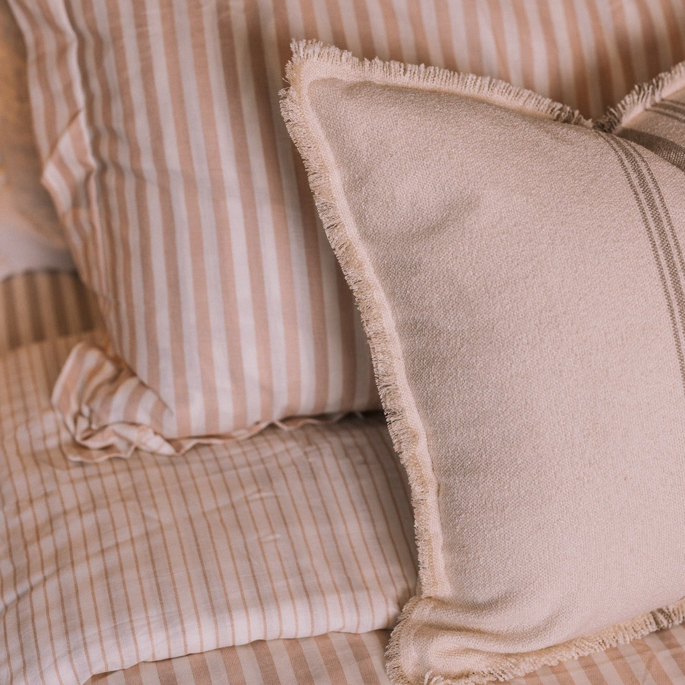 Blush pink striped bedding in a neutral bedroom with a brass bed.