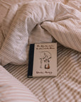 Blush pink striped bedding, unmade with a book.