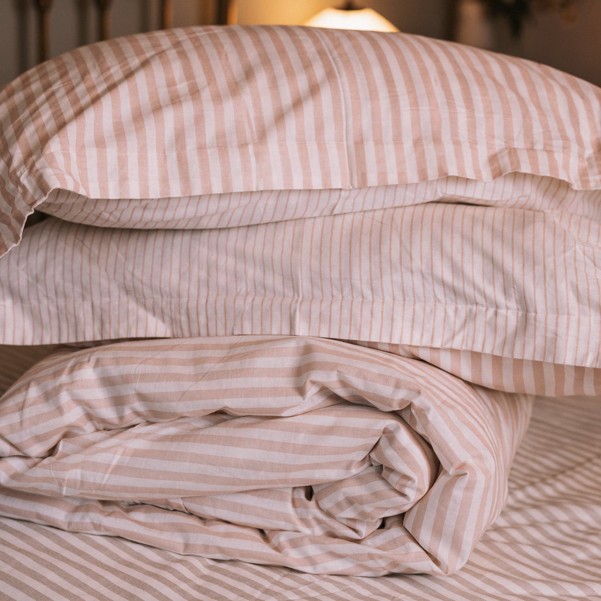 Blush pink striped bedding folded up in a neutral bedroom with a brass bed.