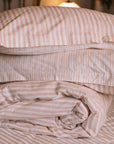 Blush pink striped bedding folded up in a neutral bedroom with a brass bed.