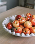 A white ceramic bobble bowl filled with red apples.
