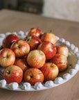 A white ceramic bobble bowl filled with red apples.