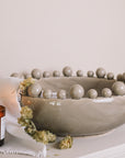 Grey ceramic bobble bowl with a lit candle and dried hops.