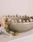 Grey ceramic bobble bowl with a lit candle and dried hops.