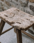 A reclaimed style wooden stool against a stone wall.
