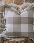 Brown and cream gingham cushion on wooden stool against a stone wall.