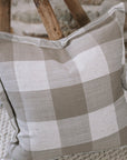 Brown and cream gingham cushion on wooden stool against a stone wall.