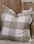 Brown and cream gingham cushion on wooden stool against a wooden wall.