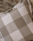 Brown and cream gingham cushion on wooden stool against a stone wall.