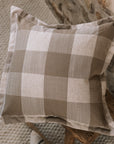 Brown and cream gingham cushion on wooden stool against a stone wall.