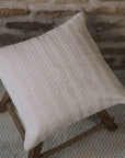 Cream and white stitch striped cushion on wooden stool against a stone wall.