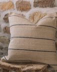 Natural cushion with black stripes on wooden stool against stone wall.