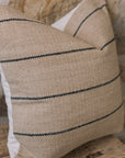 Natural cushion with black stripes on wooden stool against stone wall.