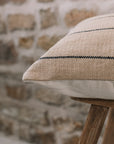 Natural cushion with black stripes on wooden stool against stone wall.