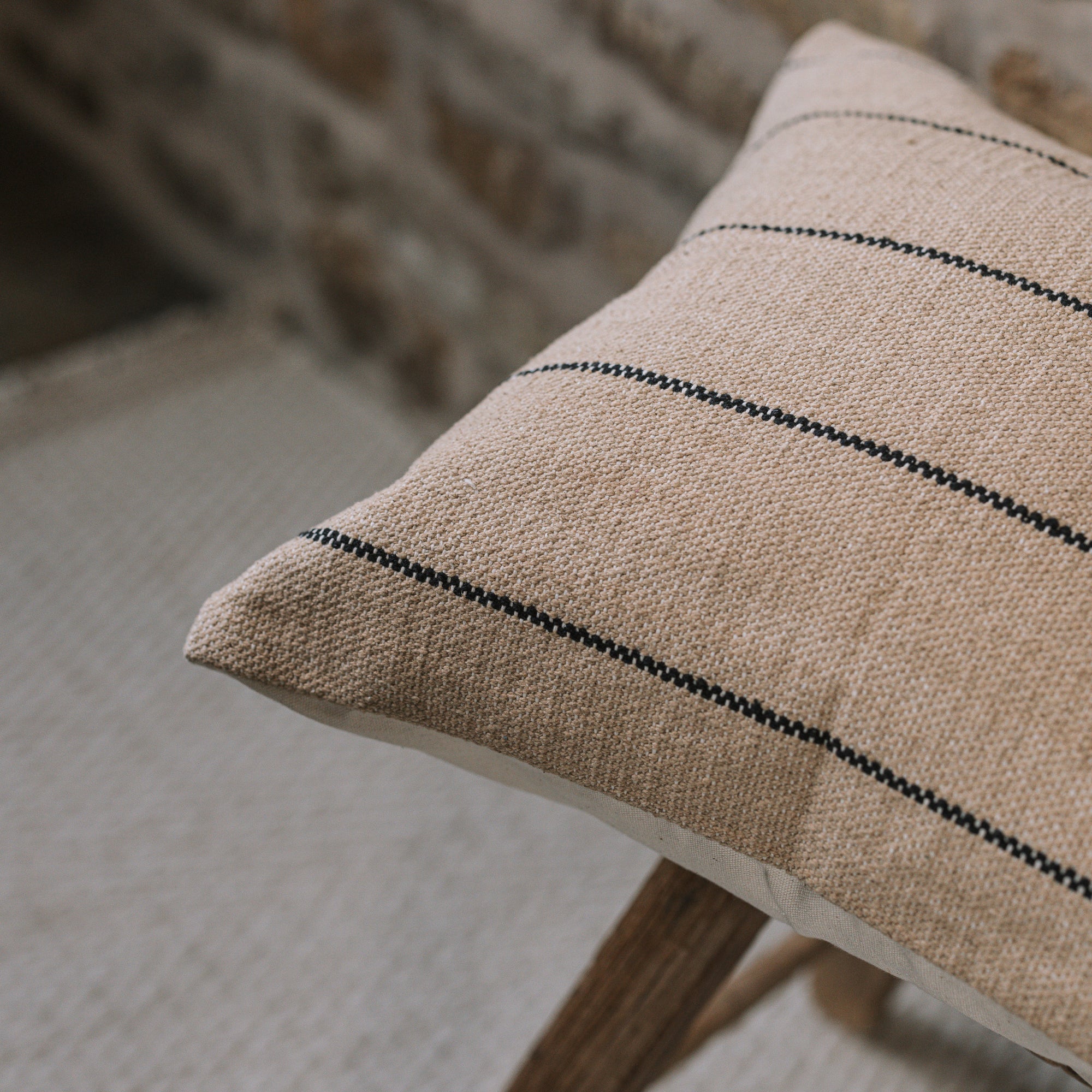 Natural cushion with black stripes on wooden stool against stone wall.