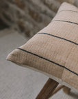 Natural cushion with black stripes on wooden stool against stone wall.