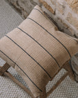 Natural cushion with black stripes on wooden stool against stone wall.