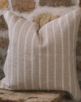 Light beige and cream stripe cushion on a wooden stool against a stone wall.