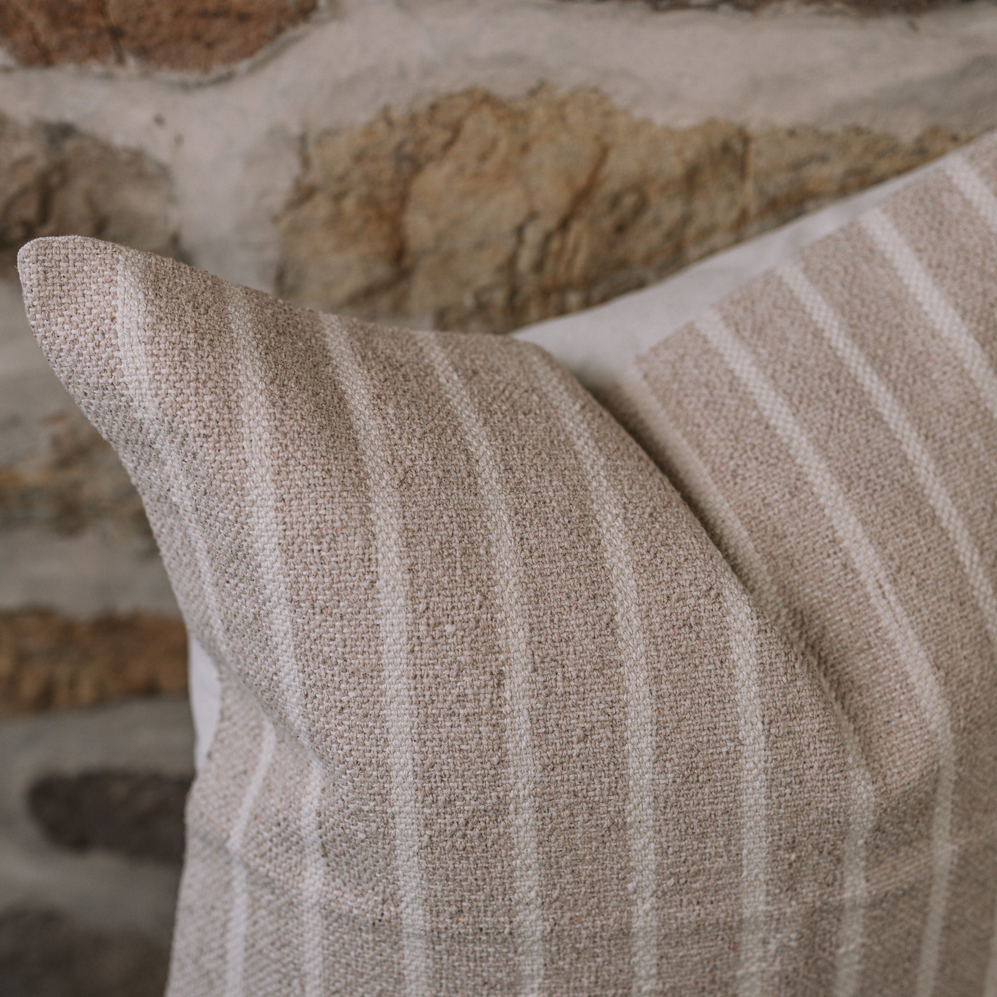 Light beige and cream stripe cushion on a wooden stool against a stone wall.