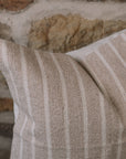 Light beige and cream stripe cushion on a wooden stool against a stone wall.