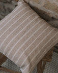 Light beige and cream stripe cushion on a wooden stool against a stone wall.