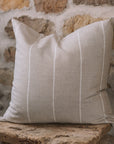 Beige and white striped cushion on a wooden stool against a stone wall.