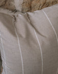 Beige and white striped cushion on a wooden stool against a stone wall.