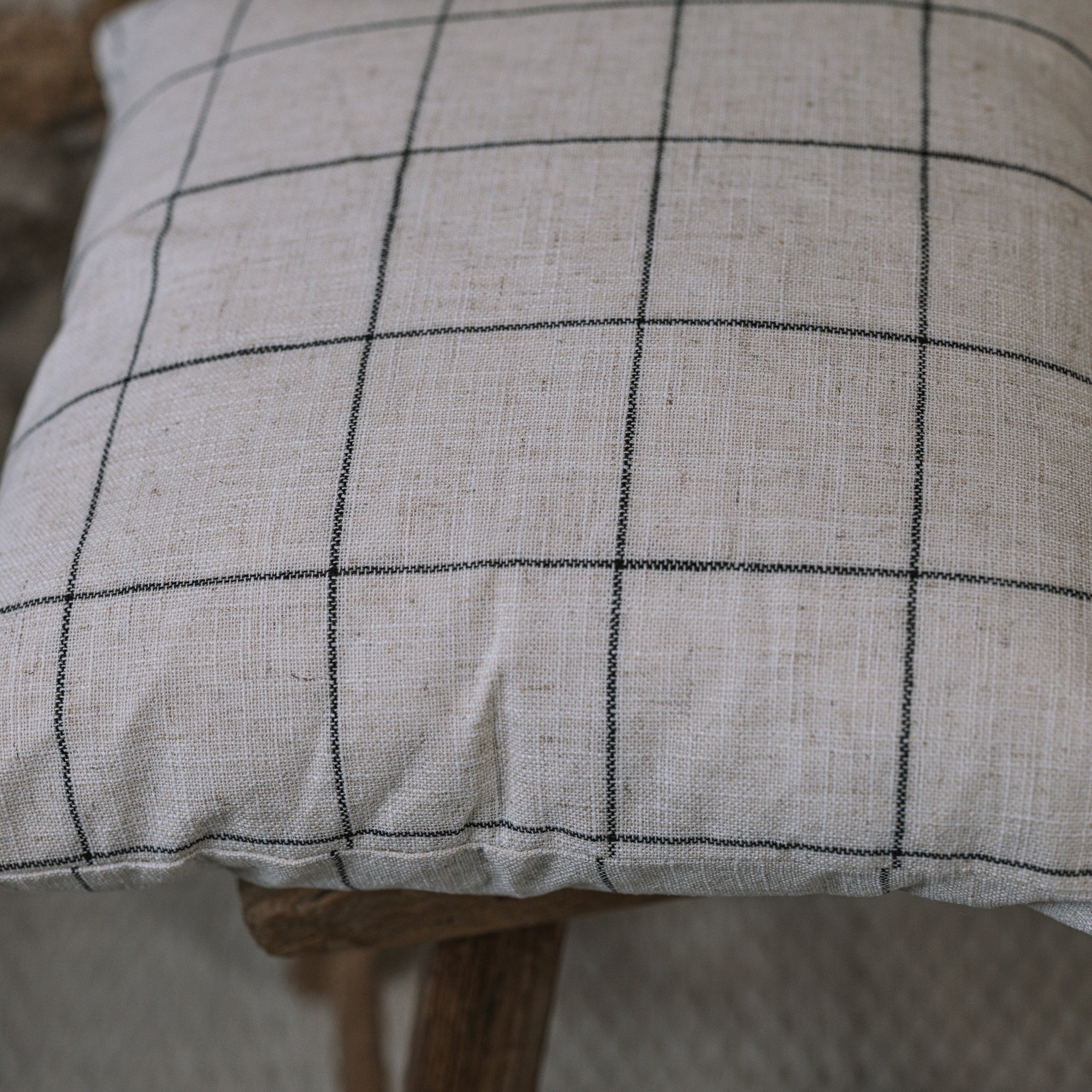 White and black grid cushion on wooden stool against a stone wall. 