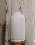 Textured White Vase against a frilly curtain.