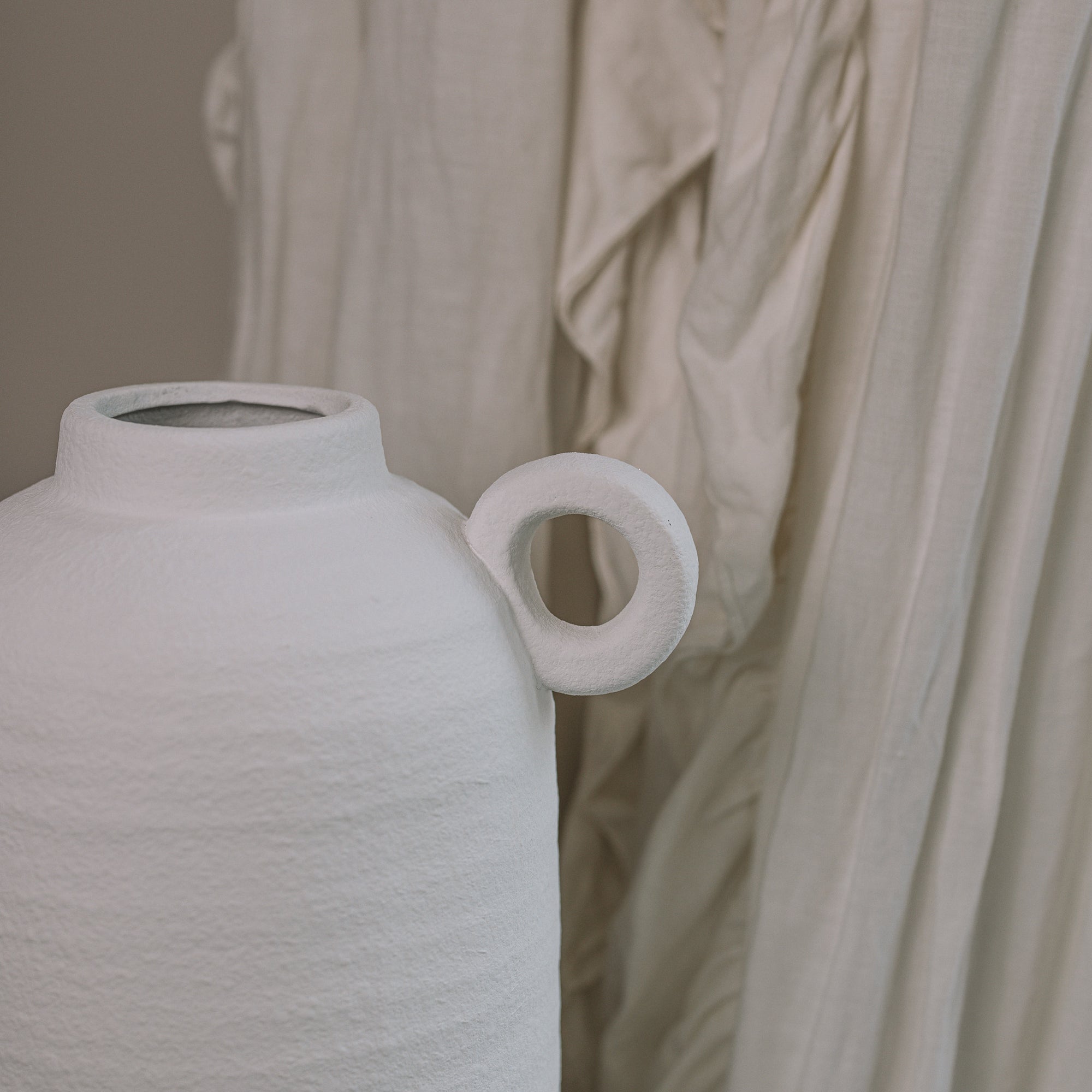 Textured White Vase against a frilly curtain. 