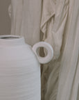 Textured White Vase against a frilly curtain. 