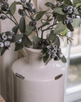 White distressed bottle vase with berry spray branches on a wooden stool.