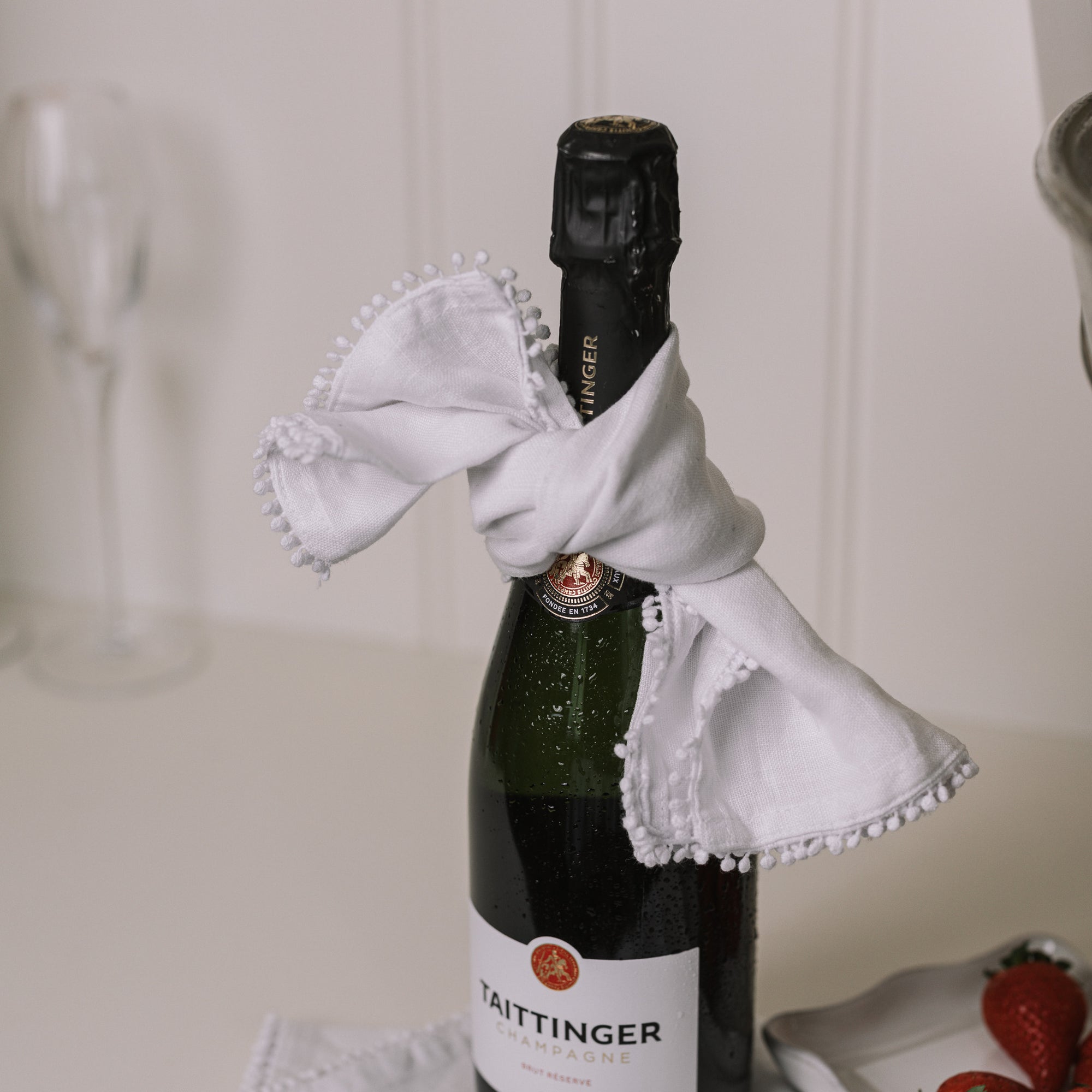 White linen napkin folded over with bobbles on the trim with champagne and strawberries.