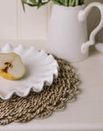 White ceramic cake plate with ruffled edges with a sliced pear on a rattan placemat.