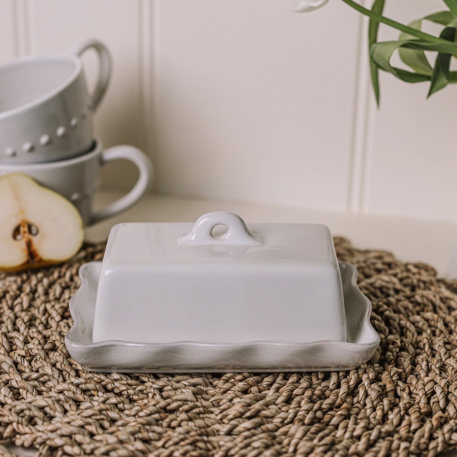 White stoneware butter dish with lid, with pie crust edge on rattan placemat.