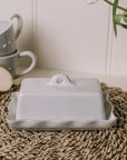 White stoneware butter dish with lid, with pie crust edge on rattan placemat.