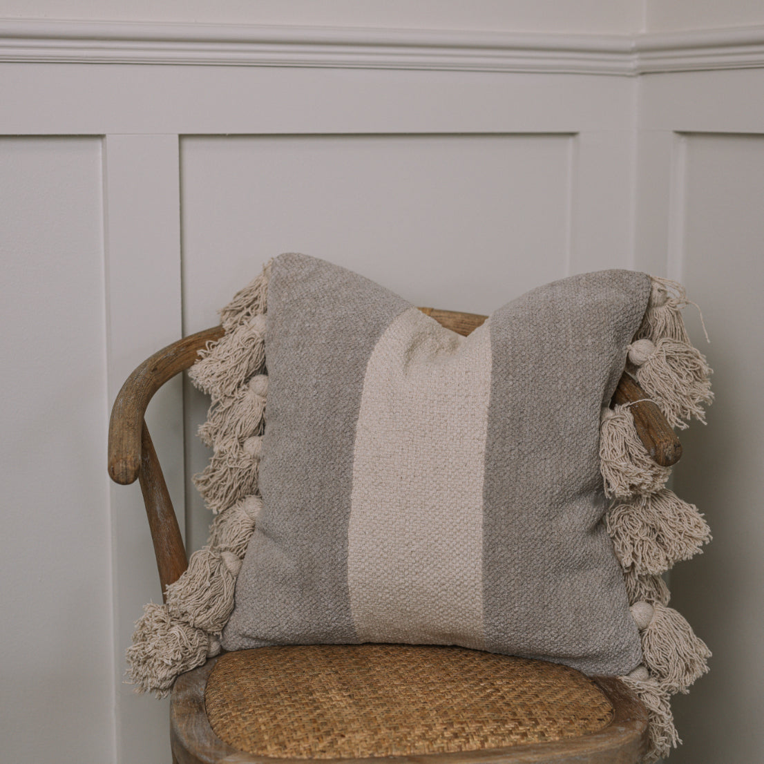 Grey and cream cushion with tassels on wicker chair.