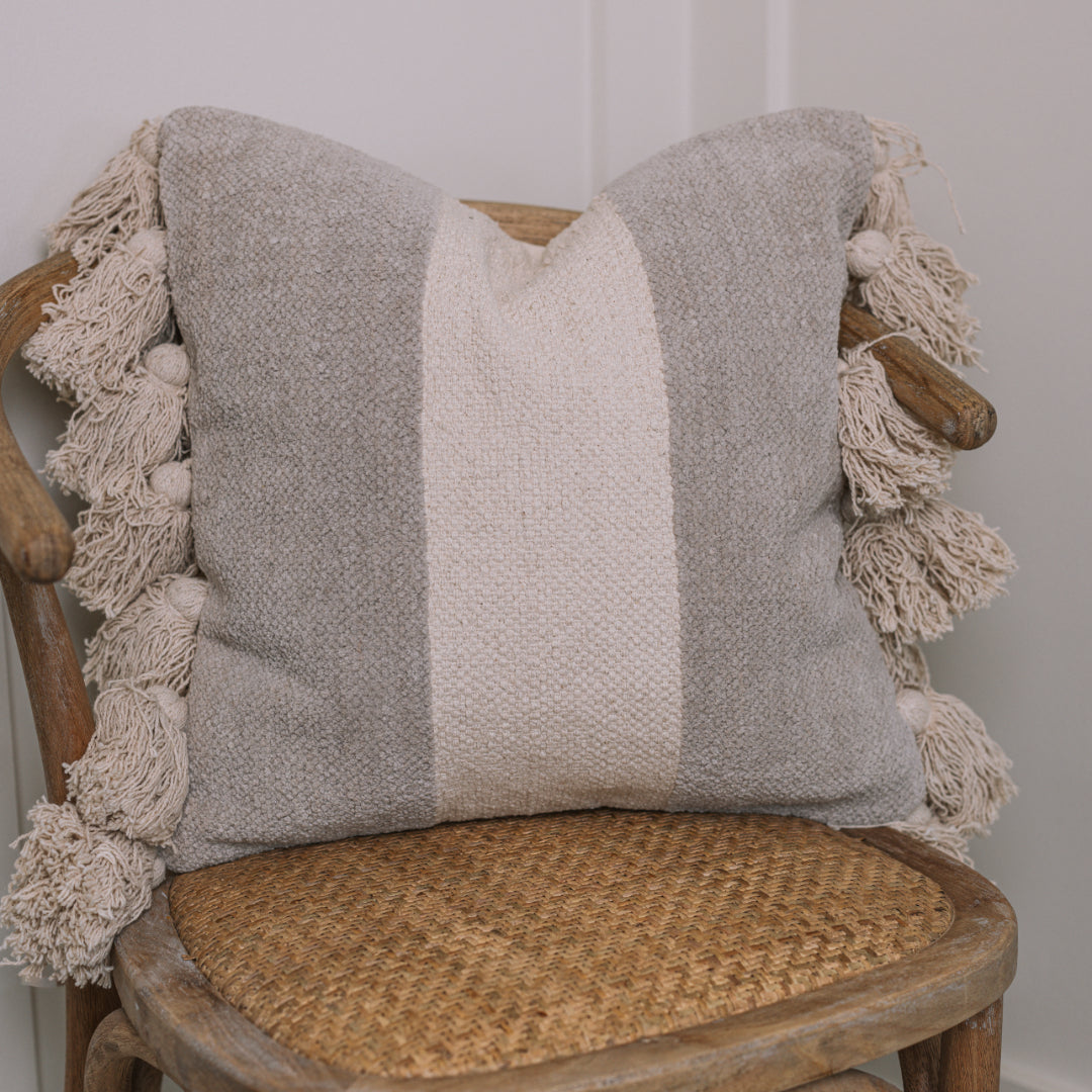 Grey and cream cushion with tassels on wicker chair.