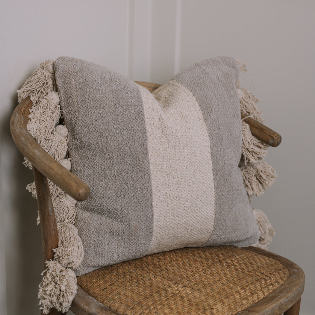 Grey and cream cushion with tassels on wicker chair.