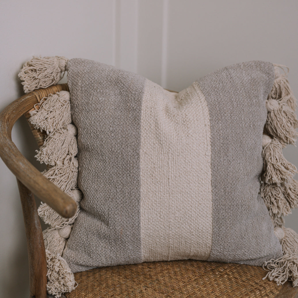 Grey and cream cushion with tassels on wicker chair.