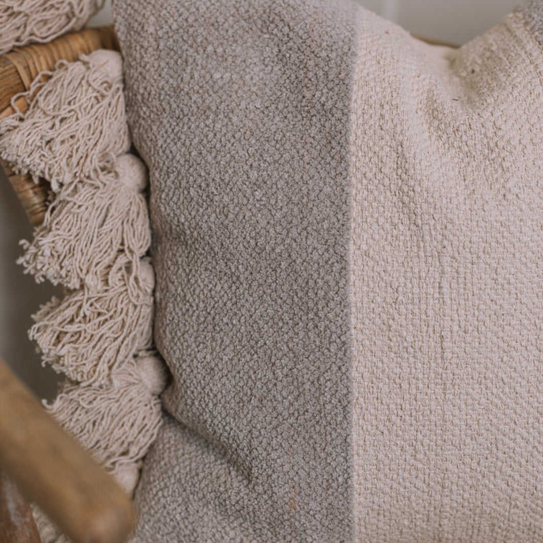 Close up of grey and cream cushion with tassels on wicker chair.