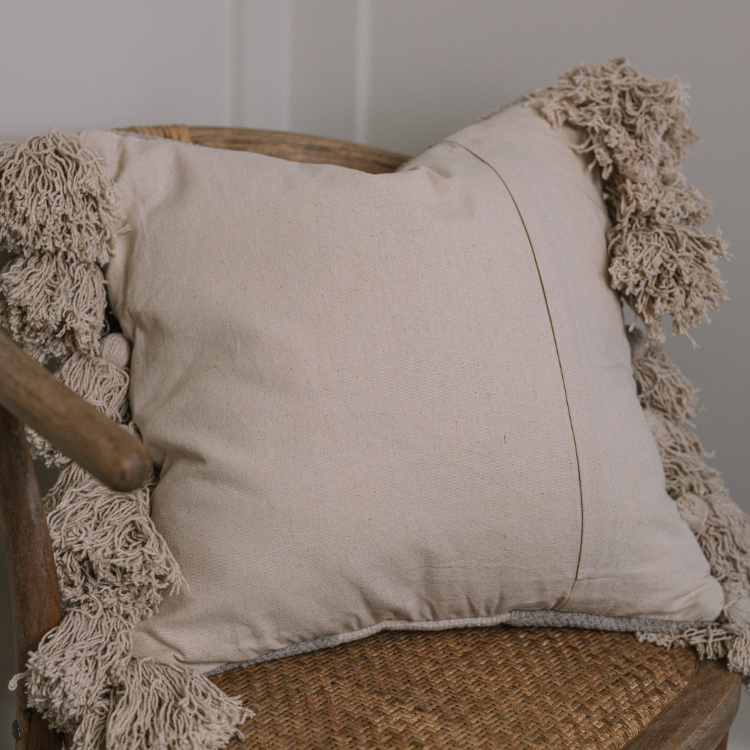 Back of cream cushion with tassels on wicker chair.