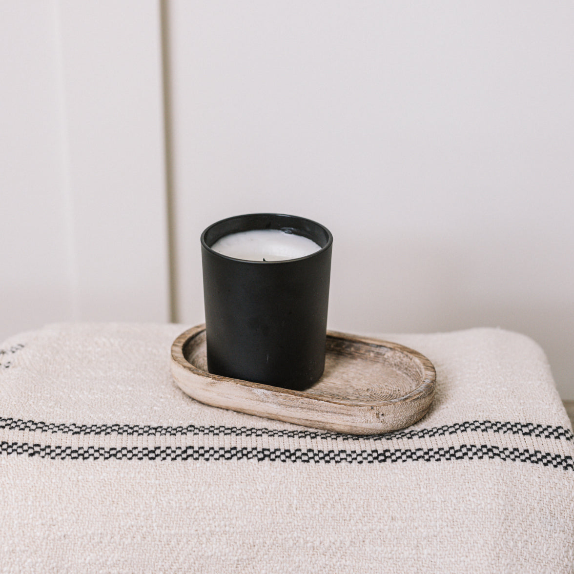 Small rustic wooden tray on cream throw, with black candle.