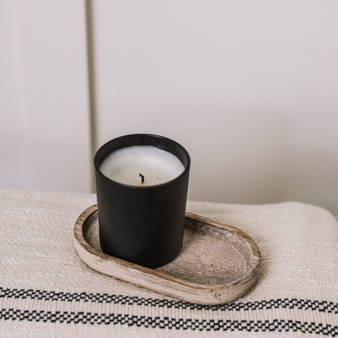 Small rustic wooden tray on cream throw with black candle.